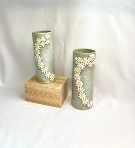Two speckled green vases with swirl of daisies