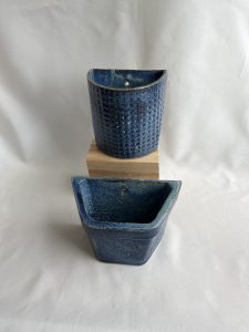 Blue, hanging flowerpots. One has a round front the other is angular